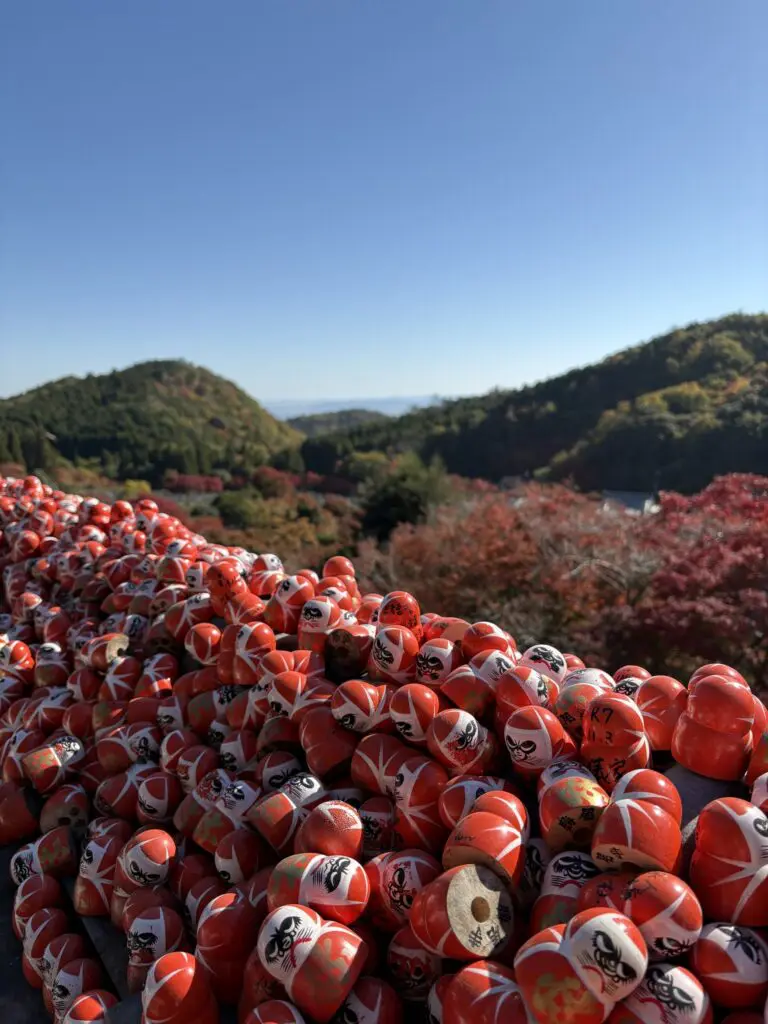 red daruma dolls with autumn hills under blue sky